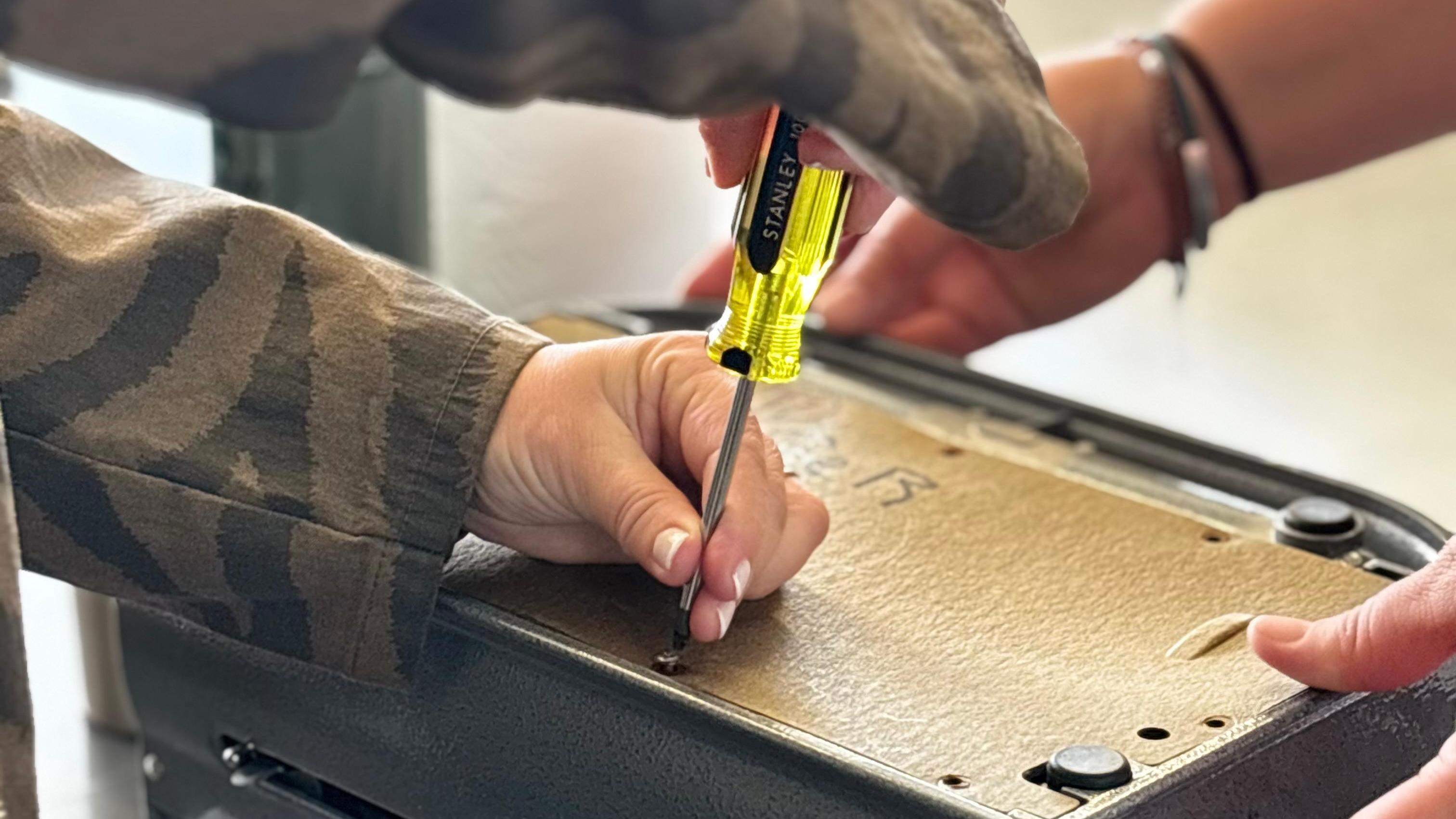 Máquina Perkins en reparación. Dos personas destornillando la tapa. 